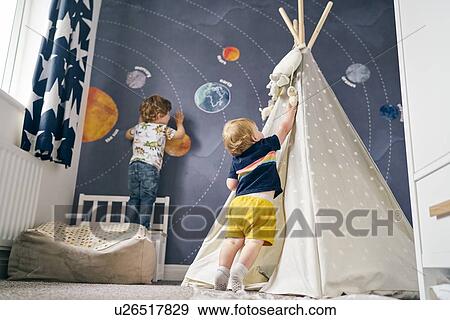 Stock Photo - Brothers playing on mural of solar system and playing in teepee at home. Fotosearch