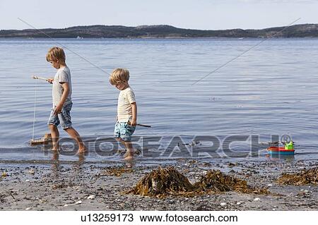 Stock Image - Brothers playing with toy boat on beach. Fotosearch