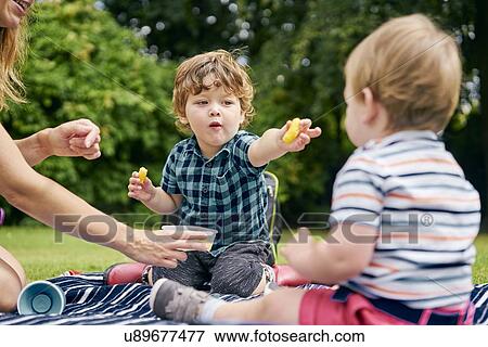 Brothers sharing food in park View Large Photo Image Stock Photo - Brothers sharing food in park. Fotosearch