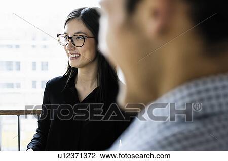 Stock Image - Businessman and businesswoman talking in corridor of building. Fotosearch
