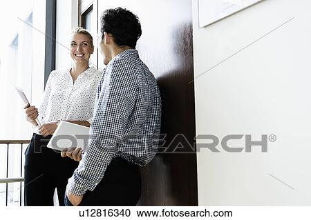 Stock Image - Businessman and businesswoman talking in corridor of building. Fotosearch