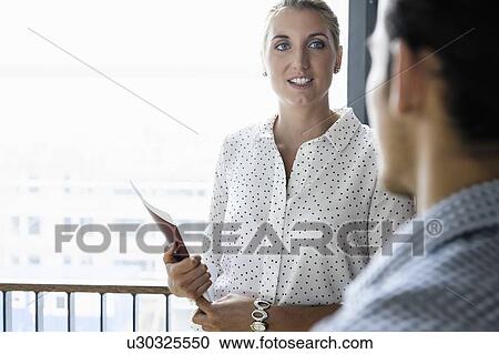Stock Image - Businessman and businesswoman talking in corridor of building. Fotosearch