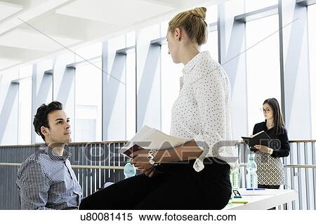 Businessman and businesswoman talking in office, colleague in background View Large Photo Image Stock Photography - Businessman and businesswoman talking in office, colleague in background. Fotosearch