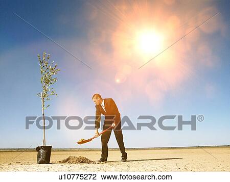 Stock Image - Businessman planting plants in desert. Fotosearch