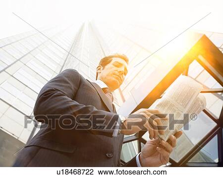 Stock Image - Businessman reading the newspaper outside office building. Fotosearch