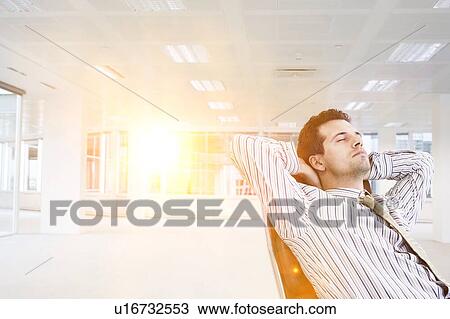 Stock Image - Businessman relaxing in chair in empty office. Fotosearch