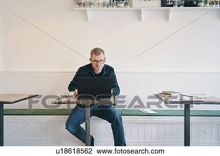 Stock Image - Businessman working on laptop in restaurant. Fotosearch