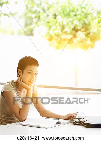 Stock Image - Businesswoman reading paperwork in home office. Fotosearch