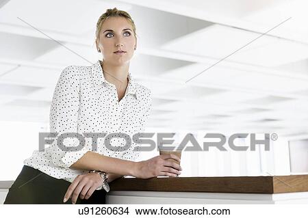 Picture - Businesswoman taking coffee break in office. Fotosearch