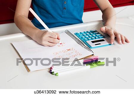Stock Image - Child doing maths homework using calculator. Fotosearch