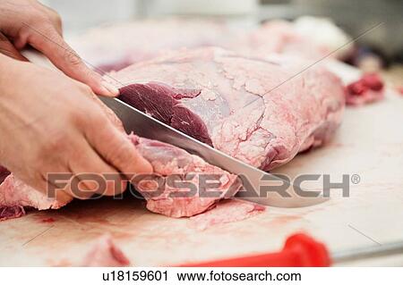 Stock Image - Close up of butcher caving piece of meat in butchers. Fotosearch