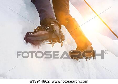 Stock Image - Close up of climber climbing ice mountain in mountainering shoes with strong lens flare. Fotosearch