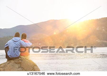 Couple hugging sitting by lake View Large Photo Image Stock Photograph - Couple hugging sitting by lake. Fotosearch