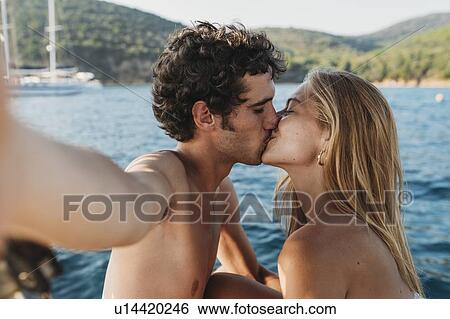 Stock Photograph - Couple taking selfie and kissing by seaside, Italy. Fotosearch