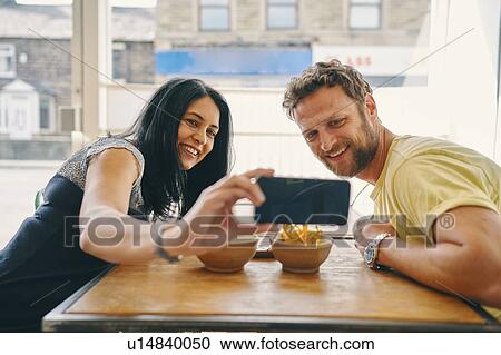 Stock Image - Couple taking selfie in restaurant. Fotosearch