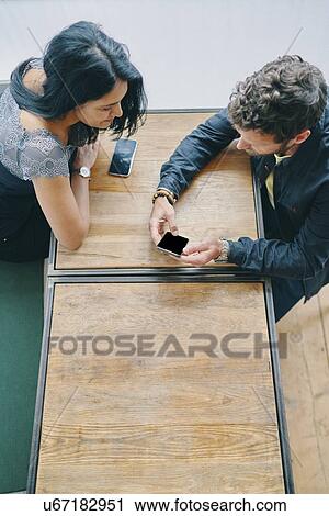 Stock Image - Couple talking and using smartphone in restaurant. Fotosearch