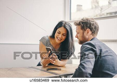 Stock Photo - Couple talking and using smartphone in restaurant. Fotosearch