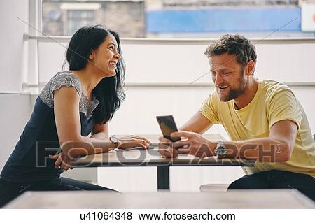 Stock Photo - Couple talking and using smartphone in restaurant. Fotosearch