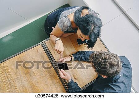 Stock Photograph - Couple talking and using smartphone in restaurant. Fotosearch