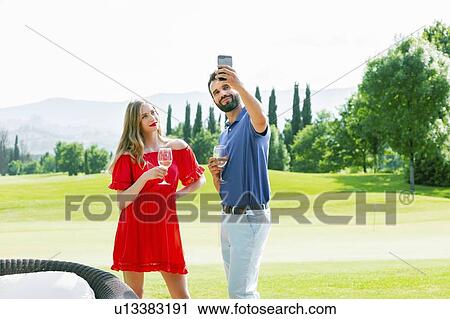 Couple with wine glasses taking selfie on golf course View Large Photo Image Stock Image - Couple with wine glasses taking selfie on golf course. Fotosearch