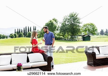 Couple with wine glasses talking beside sofa on golf course View Large Photo Image Picture - Couple with wine glasses talking beside sofa on golf course. Fotosearch