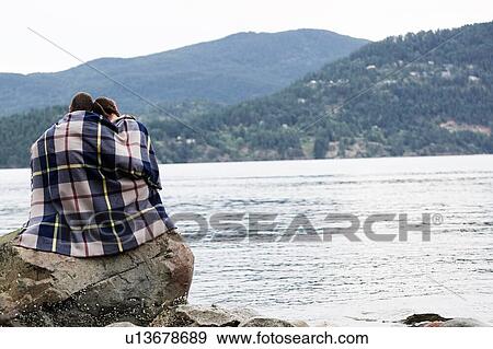 Couple wrapping in blanket sitting by lake View Large Photo Image Stock Photo - Couple wrapping in blanket sitting by lake. Fotosearch