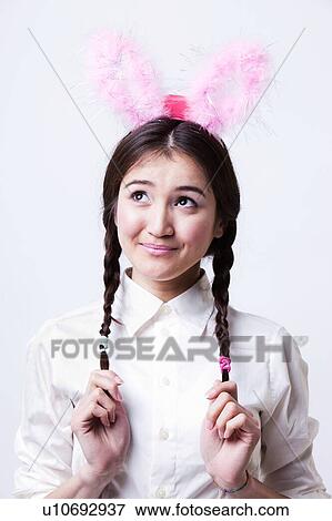 Stock Photo - Cute asian girl wearing pink bunny ears and holding braided hair. Fotosearch
