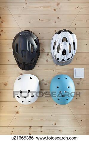 Stock Photograph - Cycling helmets for adults and children hanging on wooden wall. Fotosearch