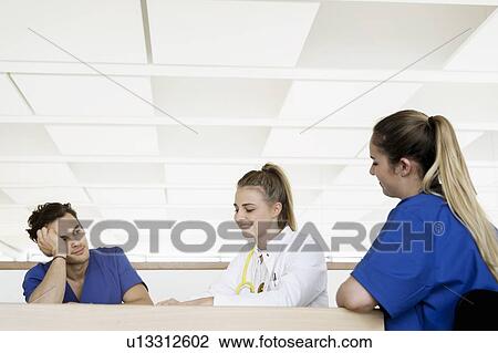 Stock Image - Doctor and nurses talking at corridor in hospital. Fotosearch