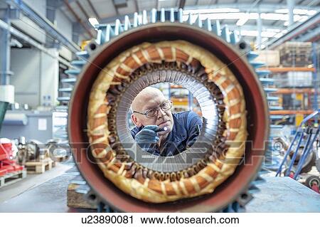 Stock Image - Electrical engineer inspecting winding on generator stator in electrical engineering factory. Fotosearch