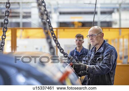 Stock Image - Engineers craning generator in electrical engineering factory. Fotosearch