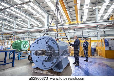 Stock Image - Engineers craning generator on to test bed in electrical engineering factory. Fotosearch