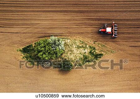 Stock Photo - Farmer and tractor with seeder, aerial view. Fotosearch