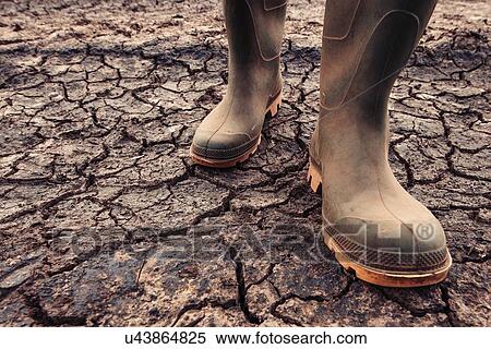 Stock Photography - Farmer in rubber boots standing on dry soil. Fotosearch
