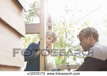 Stock Image - Father and son building treehouse together in garden. Fotosearch