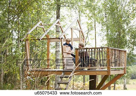 Stock Image - Father and son building treehouse together in garden. Fotosearch