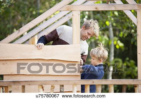 Stock Photo - Father and son building treehouse together in garden. Fotosearch