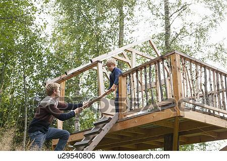 Stock Photograph - Father and son building treehouse together in garden. Fotosearch