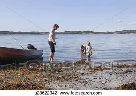 Stock Image - Father and sons playing beside boat moored on beach, Norway. Fotosearch