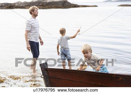 Stock Photography - Father and sons playing beside boat moored on beach, Norway. Fotosearch