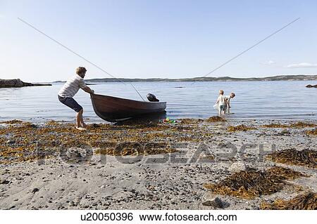 Stock Photograph - Father pulling boat onto beach, sons playing nearby, Norway. Fotosearch