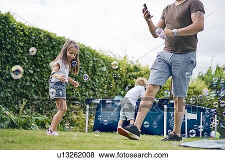 Stock Photo - Father walking past children playing in garden. Fotosearch
