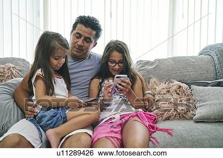 Stock Photograph - Father watching daughters play computer games on cellphone. Fotosearch