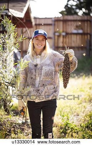 Picture - Female beekeeper holding swarm of bees. Fotosearch