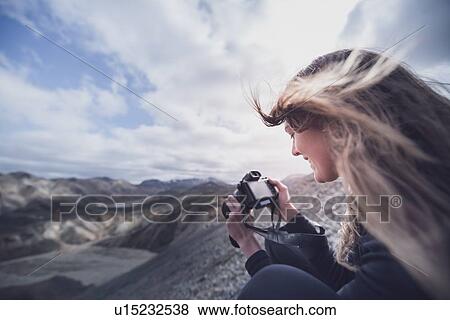 Stock Photo - Female photographer with wind blown hair taking photograph on edge of volcano, Landmannalaugar, Iceland. Fotosearch