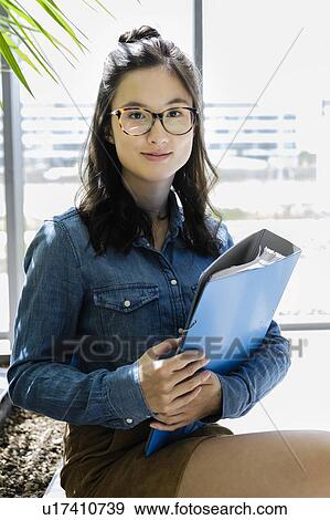 Stock Photo - Female student carrying file beside glass wall of office building. Fotosearch