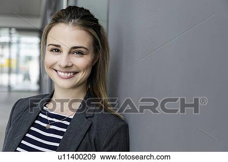 Stock Photo - Female student leaning against grey wall in office building. Fotosearch