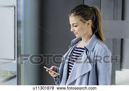 Stock Photo - Female student using smartphone at corridor of office building. Fotosearch