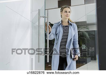 Female student with notebook opening glass door of office View Large Photo Image Stock Photograph - Female student with notebook opening glass door of office. Fotosearch