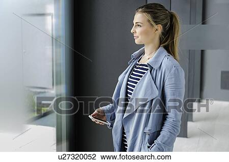 Stock Image - Female student with smartphone at corridor of office building. Fotosearch